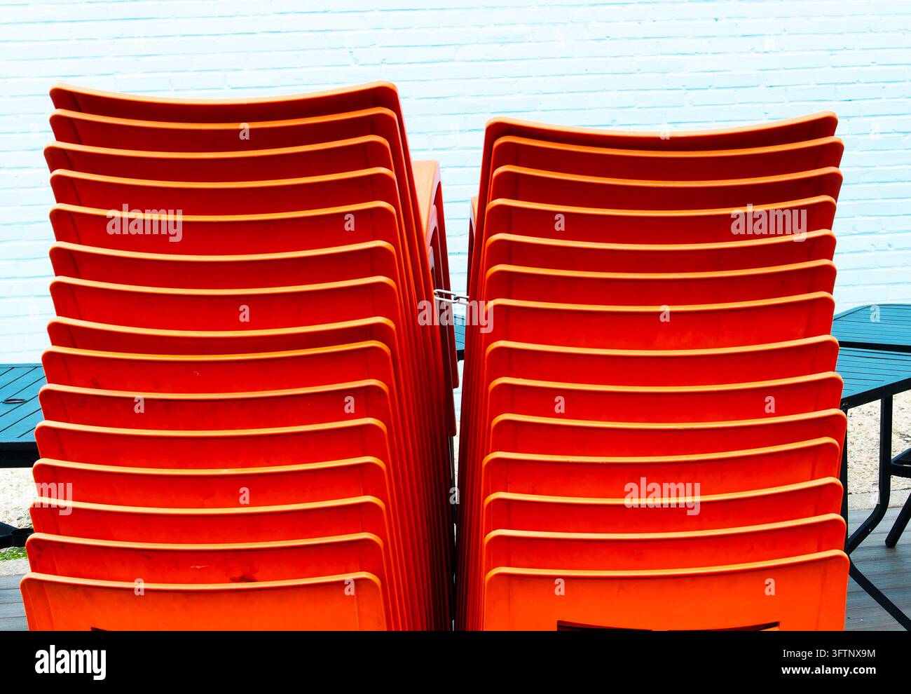 Deux hauts empilements de chaises de restaurant empilables en plastique moulé orange vif posés contre un mur de briques bleu clair Banque D'Images