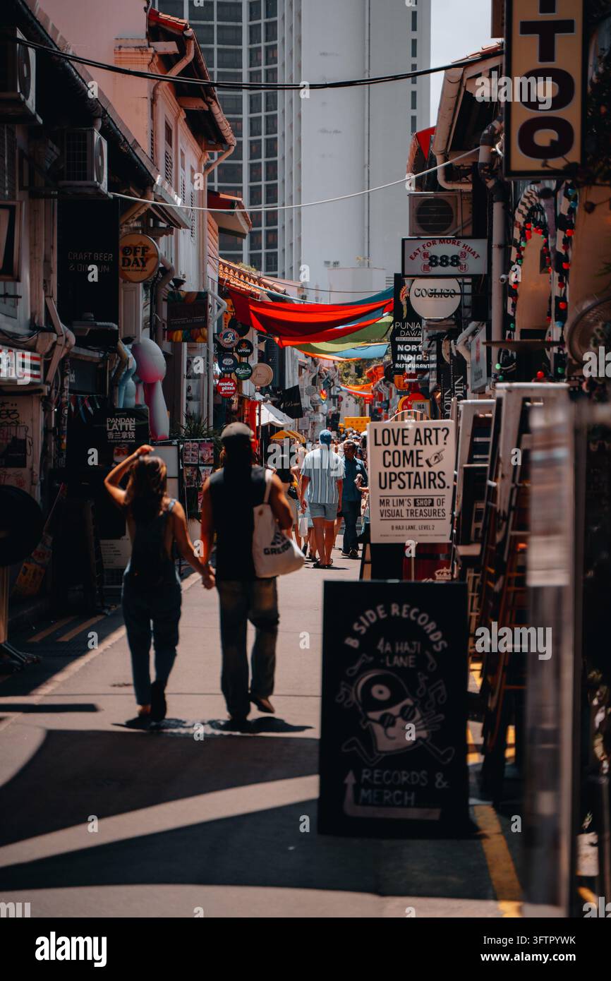 Un couple descend Haji Lane devant des boutiques et des panneaux colorés à Kampong Glam, Singapour Banque D'Images