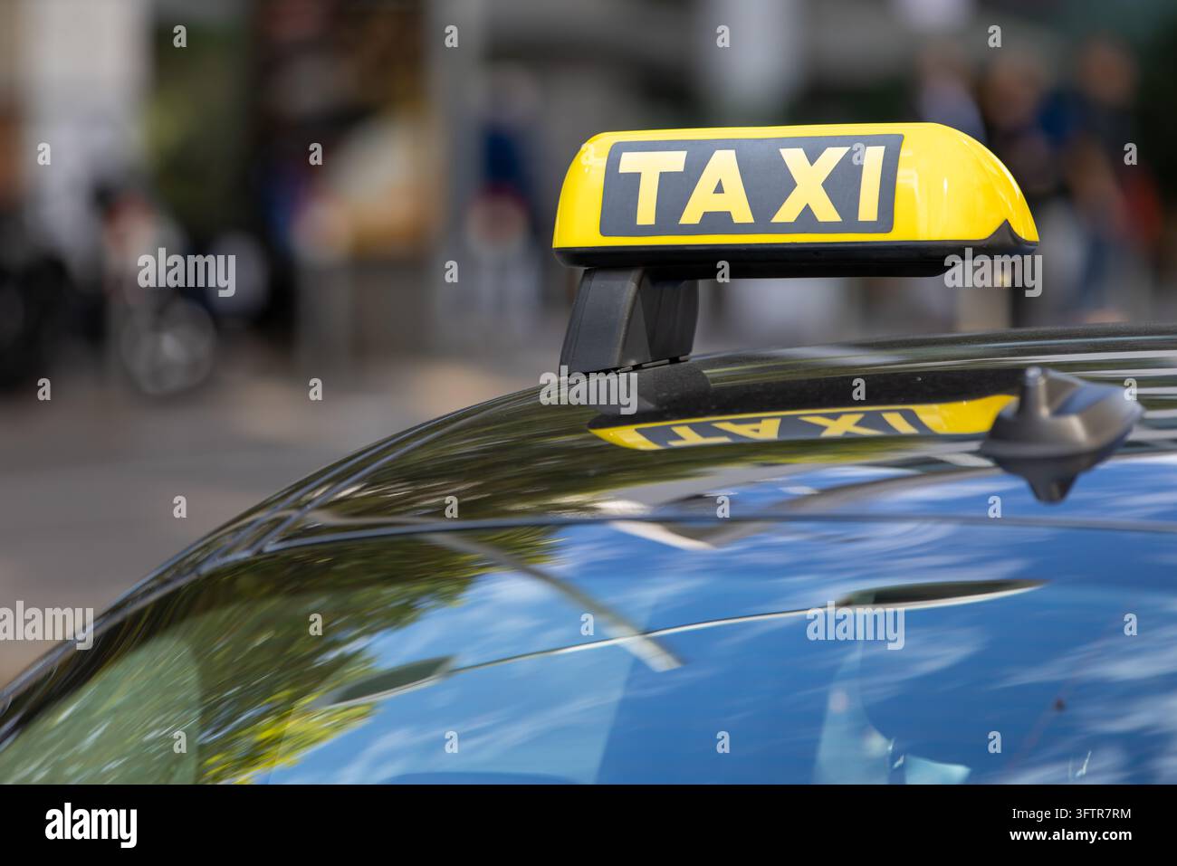 Panneau de taxi jaune monté sur le toit d'une voiture noire dans un cadre urbain Banque D'Images