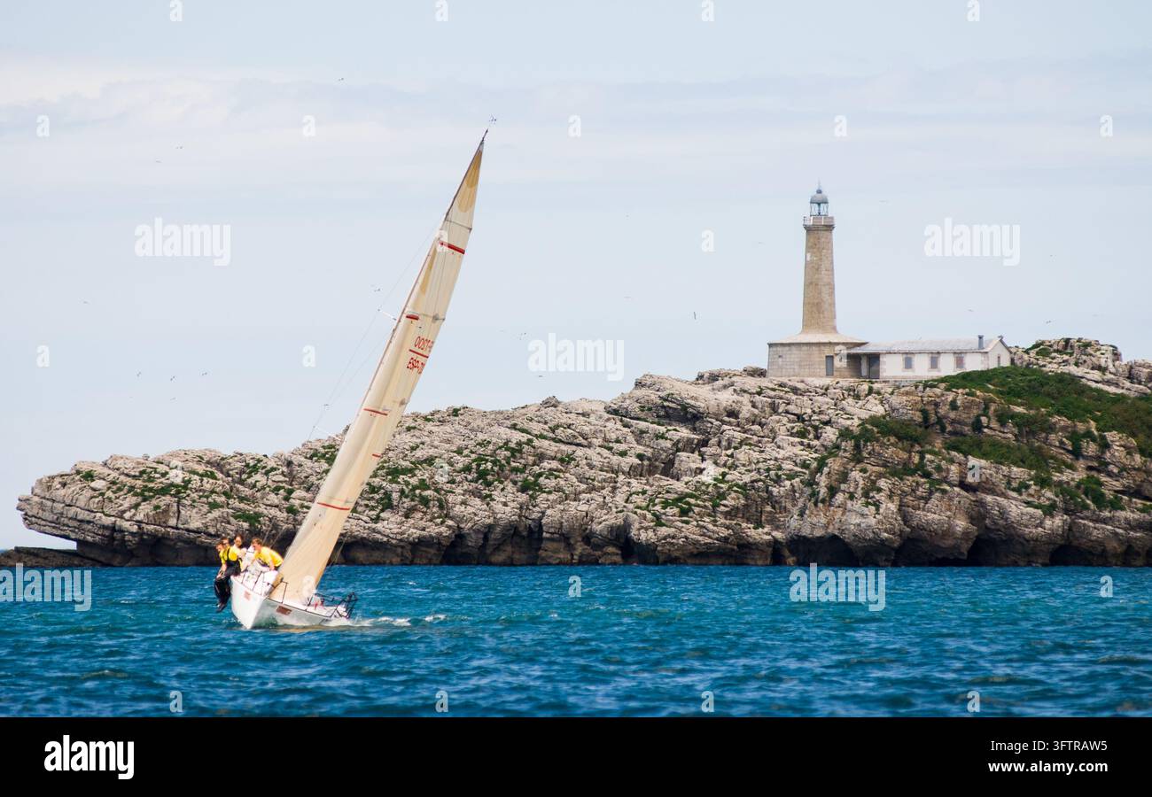 Yacht à voile et équipage passant le phare de Cabo Mayor au large de Santander, Cantabrie, Espagne. Banque D'Images
