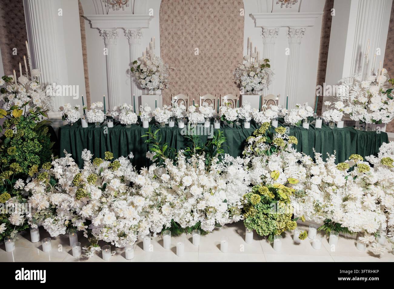 Table de banquet avec centres de table floraux blancs, draperie verte et décoration de bougies dans une scène de cadre classique pour réception de mariage ou mise en place d'événement formel Banque D'Images