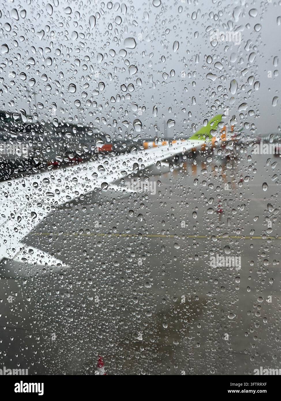 Gouttes de pluie sur le verre de la fenêtre d'avion avec l'aile sur un fond flou de la piste de l'aéroport. Des gouttelettes d'eau recouvrent une fenêtre d'avion qui donne sur un blanc - Image de stock capturée avec un smartphone