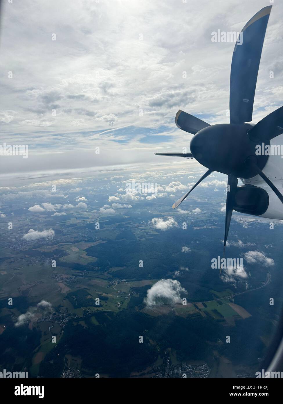 Vue d'un moteur à hélice d'avion regardant par-dessus la campagne et les nuages depuis la fenêtre. Un moteur à hélice d'avion en silhouette contre un ciel nuageux dramatique - Image de stock capturée avec un smartphone