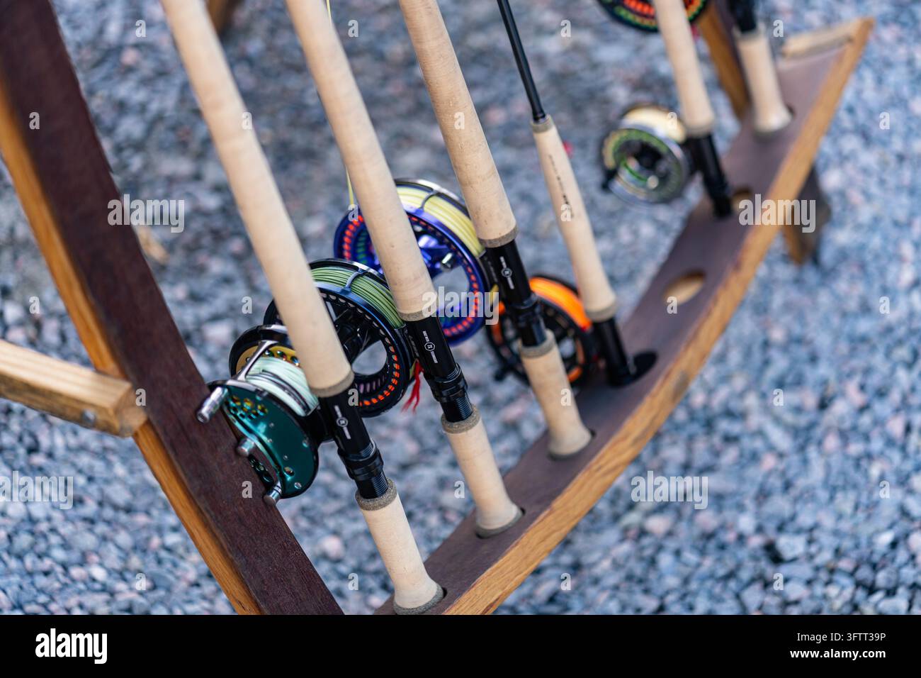 Cannes à pêche au mouche avec manches en liège et moulinets colorés rangés debout dans un support en bois fabriqué à partir de planches de tonneau de chêne sur du gravier Banque D'Images