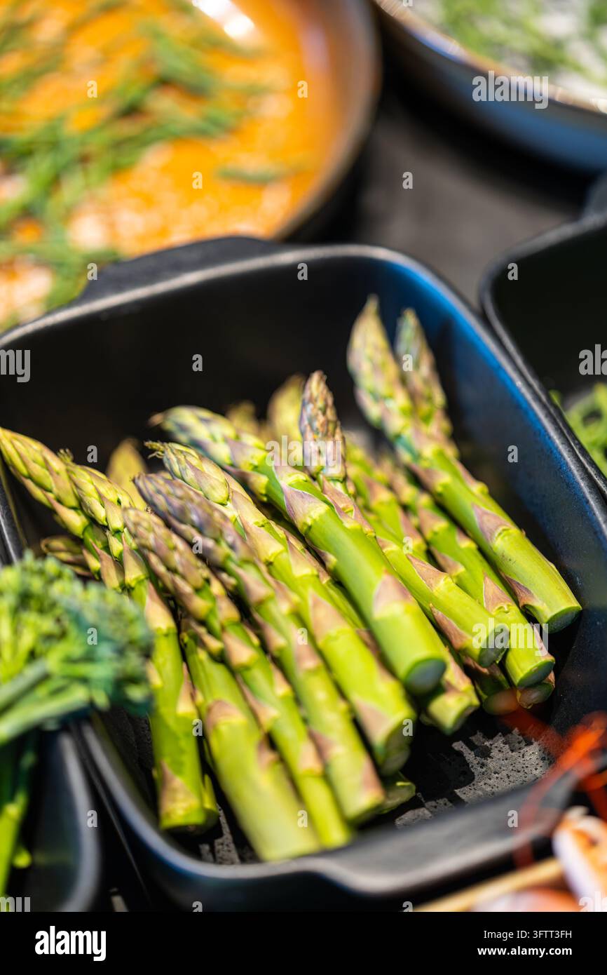 Épis d'asperges vertes fraîches dans un plat en céramique noire, avec du brocoli tendre et du samphire flous en premier plan et en arrière-plan Banque D'Images