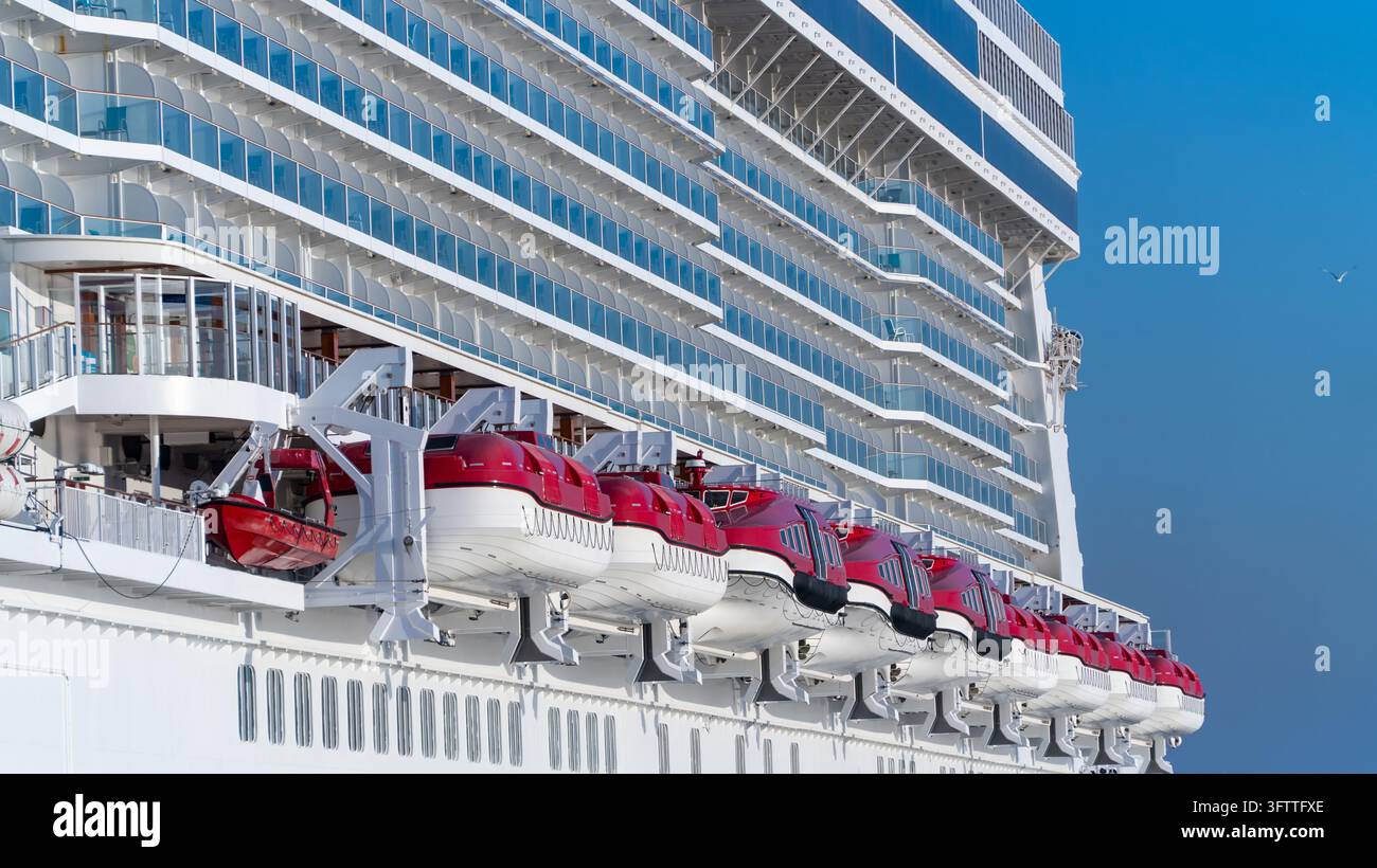 Canots de sauvetage d'un navire de croisière, une rangée de canots de sauvetage rouges et blancs sur des davits sous de nombreux ponts de cabines avec balcons sur un grand navire de croisière, contre un ciel bleu clair Banque D'Images