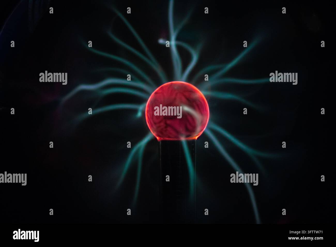 Grossissement d'un globe à plasma lumineux présentant un centre rouge vif émettant des filaments de gaz ionisé bleu électrique et cyan sur un fond noir Banque D'Images