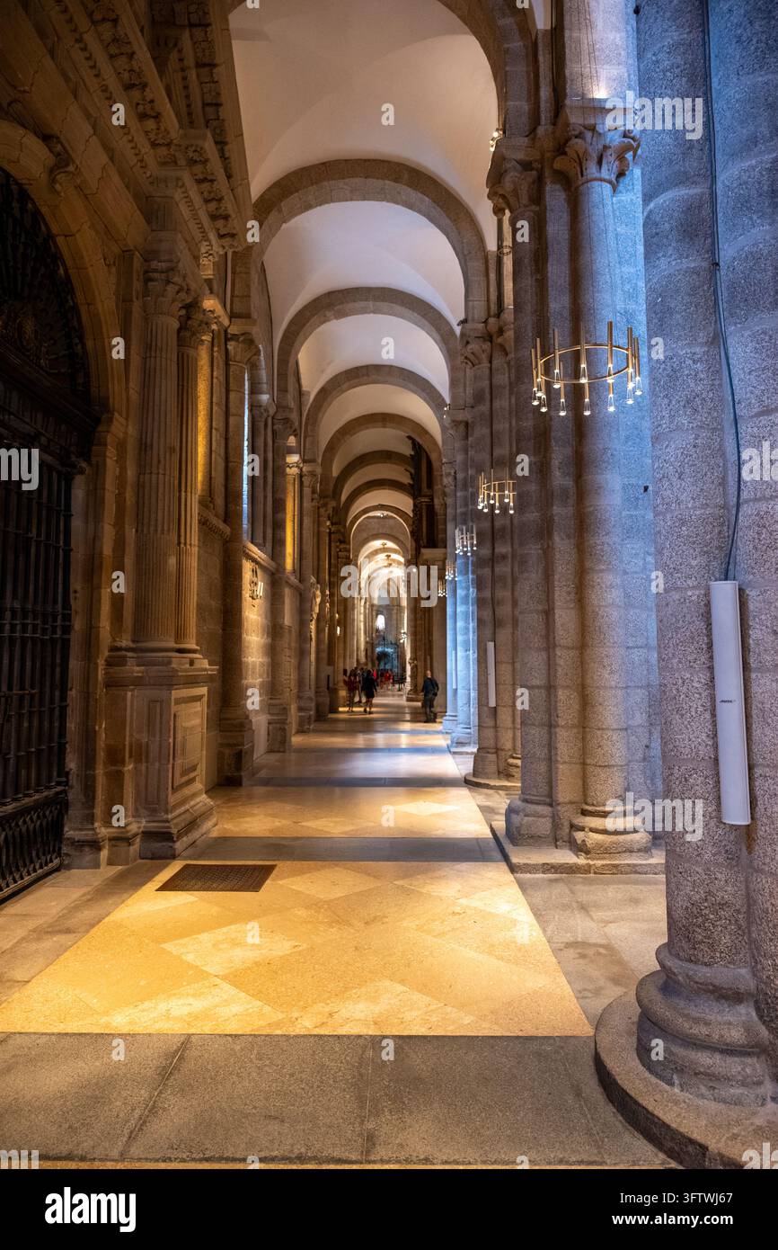 Longue perspective d'une allée cathédrale romane avec de massifs piliers en pierre, des arcs voûtés et des visiteurs à l'intérieur de la cathédrale de Saint-Jacques-de-Compostelle Banque D'Images