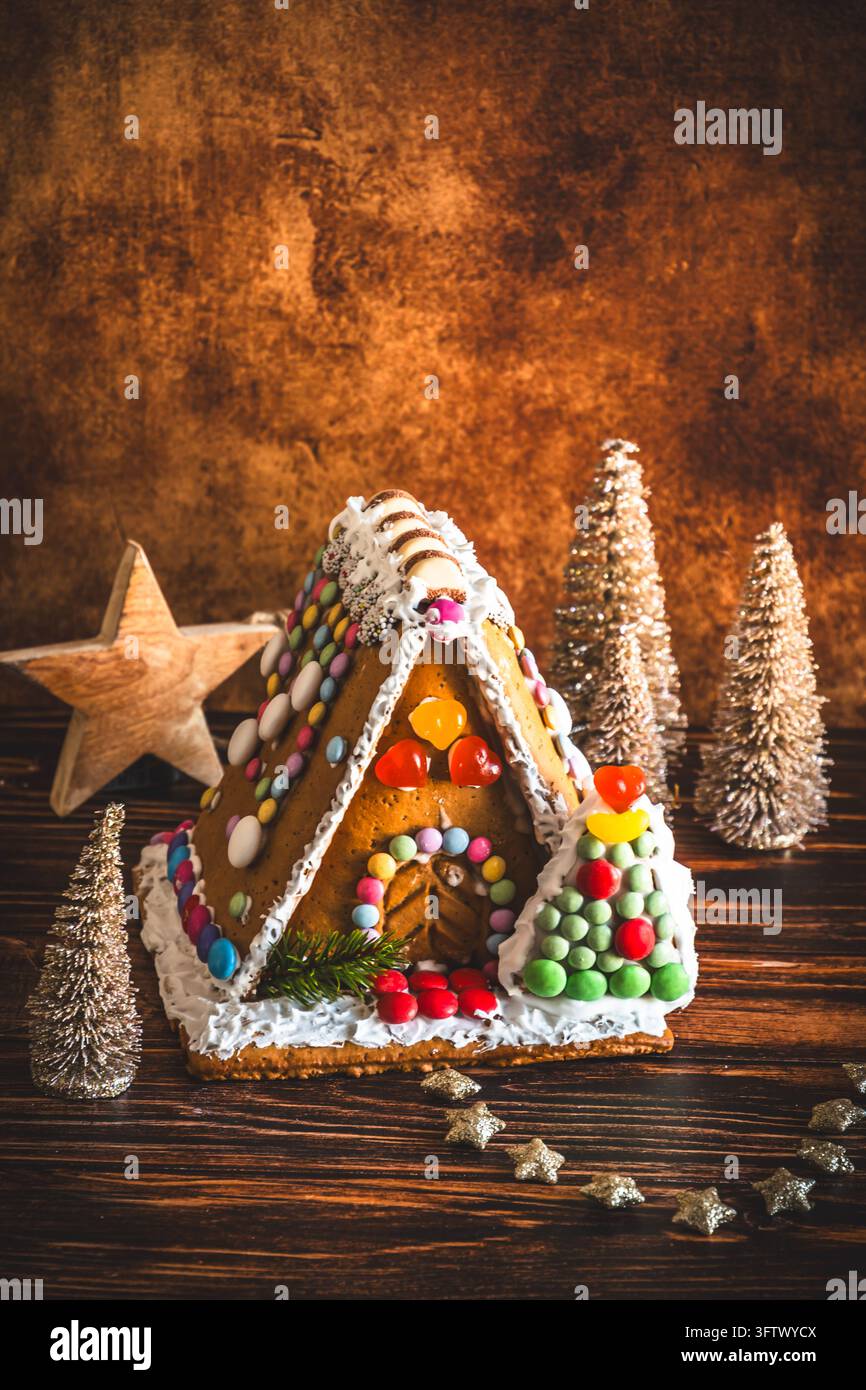 Maison en pain d'épice décorée de bonbons colorés et décoration de noël sur fond de bois, verticale avec espace copie Banque D'Images