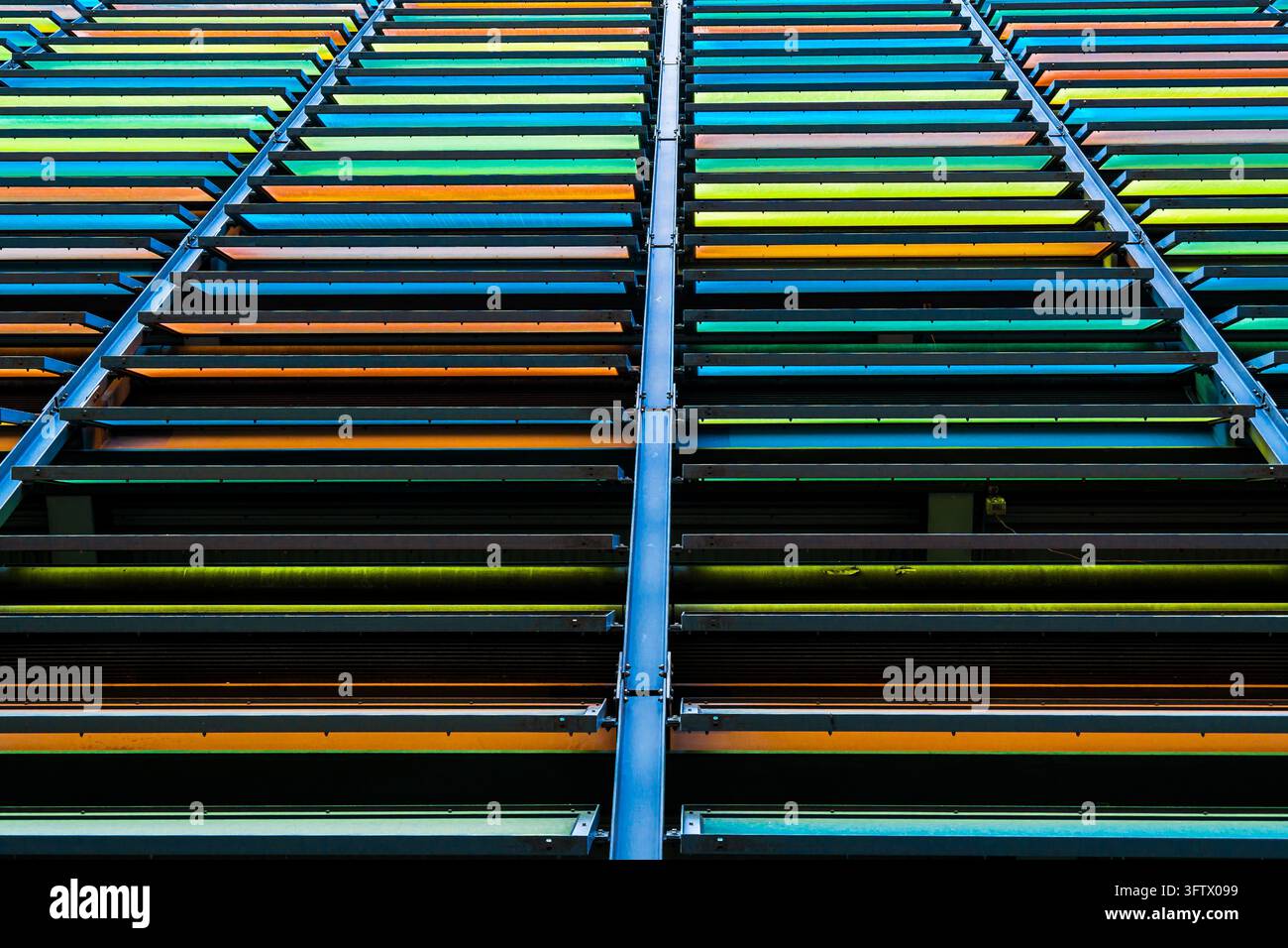 Des rangées de persiennes horizontales colorées forment un écran géométrique sur une façade de bâtiment moderne. Les lamelles bleues, vertes, jaunes et orange contrastent avec le sombre Banque D'Images