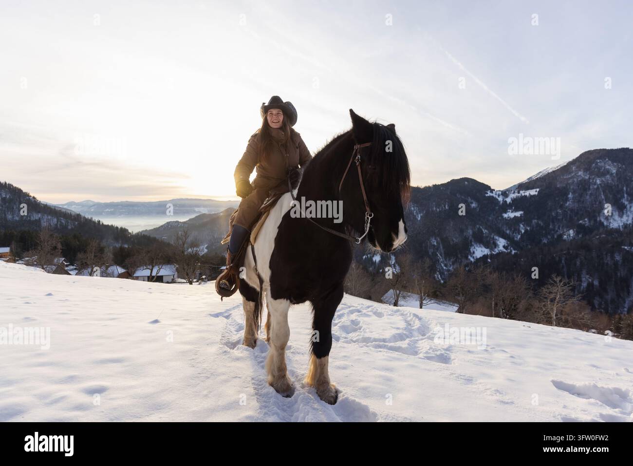 Femme à cheval dans la neige profonde des montagnes au coucher du soleil, explorant le paysage hivernal lors d'une expérience inoubliable. Banque D'Images