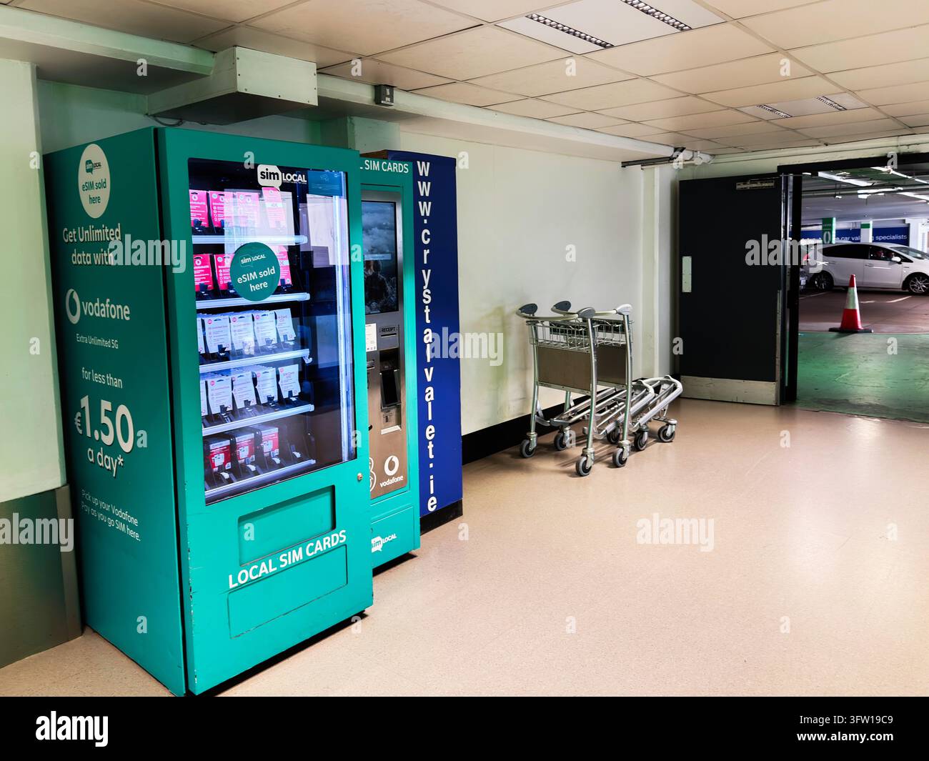 Dublin, Irlande – 23 mai 2026 : Distributeur de SIM turquoise vif à côté des chariots à bagages dans un parking intérieur calme de Dublin près des installations de l'aéroport. Banque D'Images
