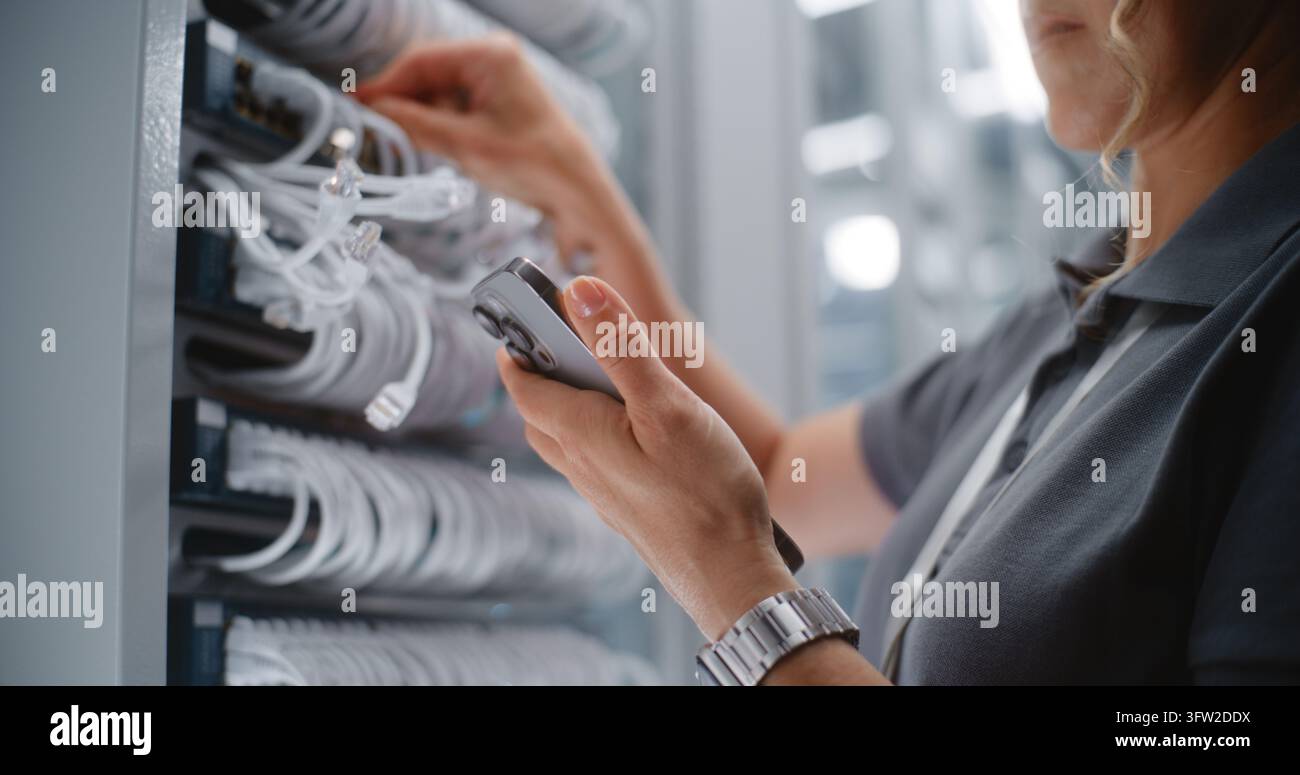 Technicienne de réseau féminine effectuant un audit physique des ports à côté d’un rack de serveurs, utilisant un smartphone pour vérifier l’identification des câbles et les enregistrements réseau. Concept de maintenance de l’infrastructure du centre de données. Banque D'Images