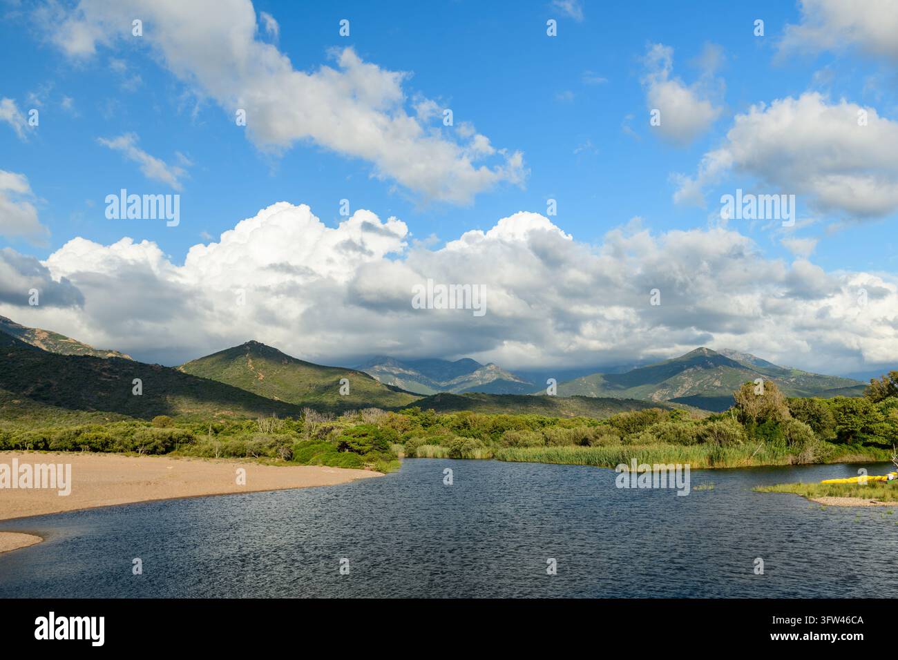 L'embouchure de la rivière Fango près de Galeria montre des eaux calmes, des berges sablonneuses et une végétation verte. Des montagnes s'élèvent sous un ciel bleu nuageux. Banque D'Images