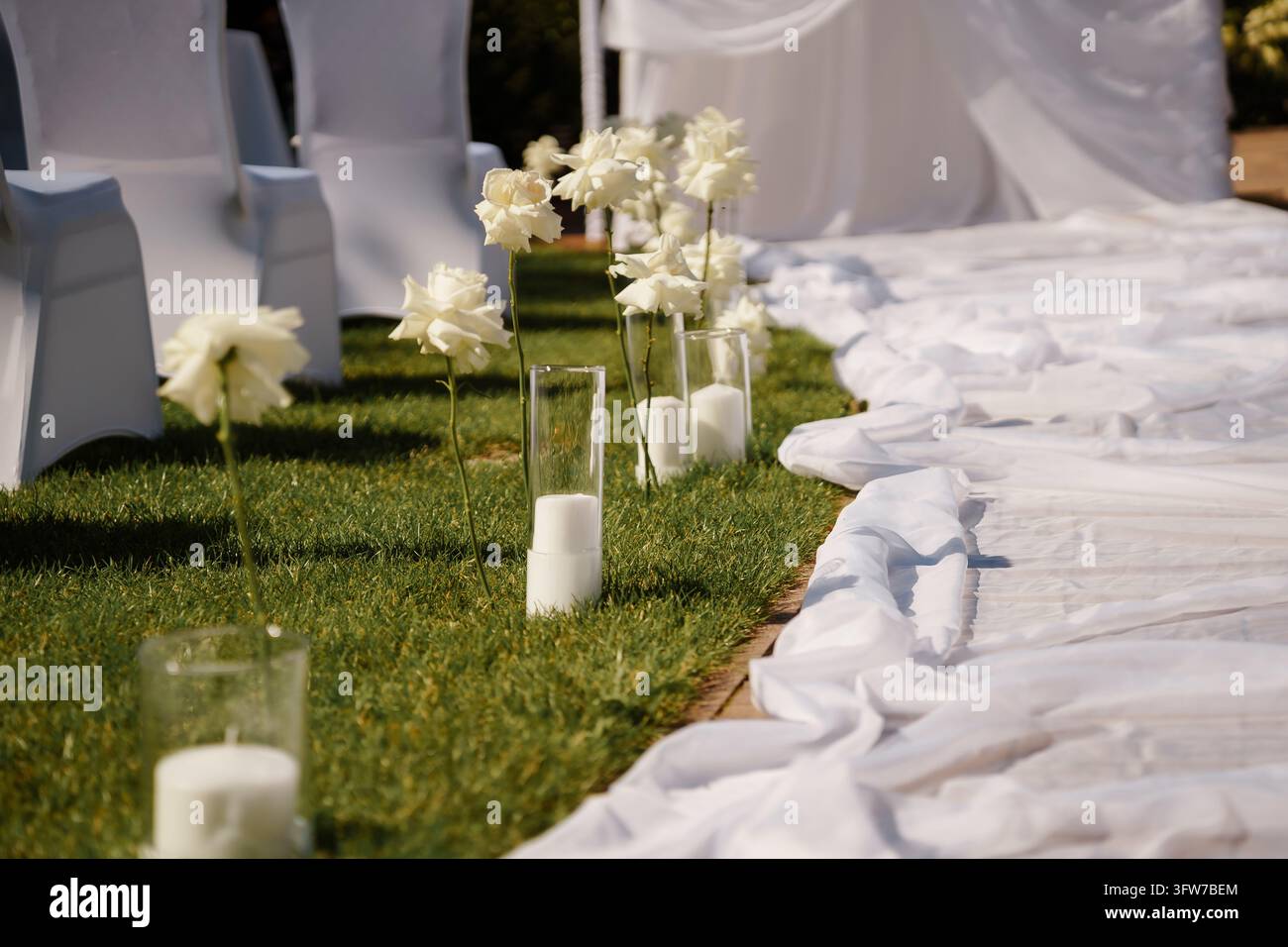 Allée élégante pour une cérémonie de mariage en plein air avec des fleurs blanches, des bougies en pilier de verre et des nappes en tissu blanc sur une pelouse verte Banque D'Images