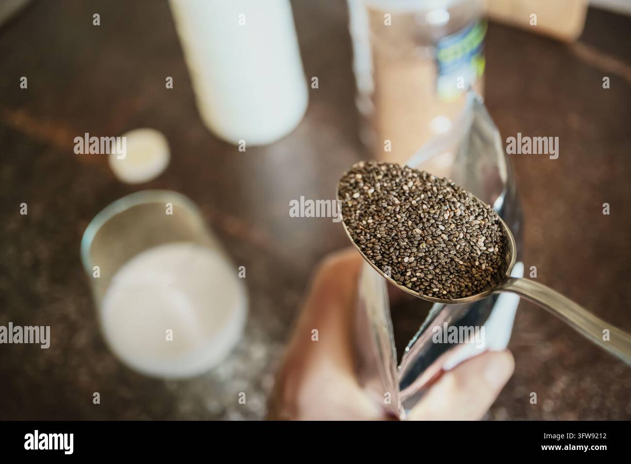 Main masculine tenant une cuillère pleine de graines de chia au-dessus d'un verre de lait en préparant des aliments sains Banque D'Images