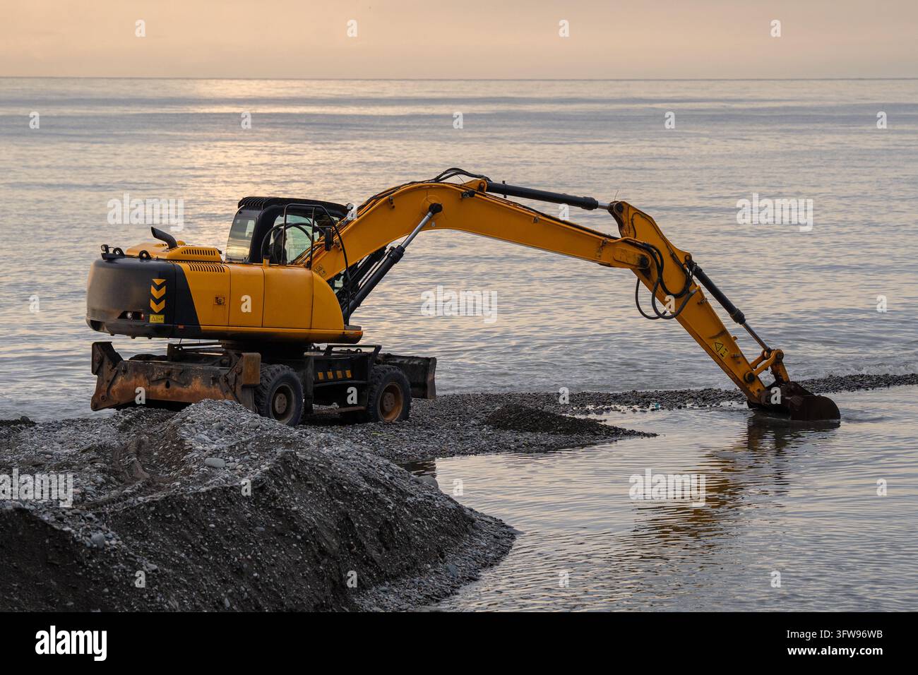 Excavatrice lourde approfondissant le chenal fluvial côtier bloqué par la boue et les pierres après des précipitations prolongées Banque D'Images