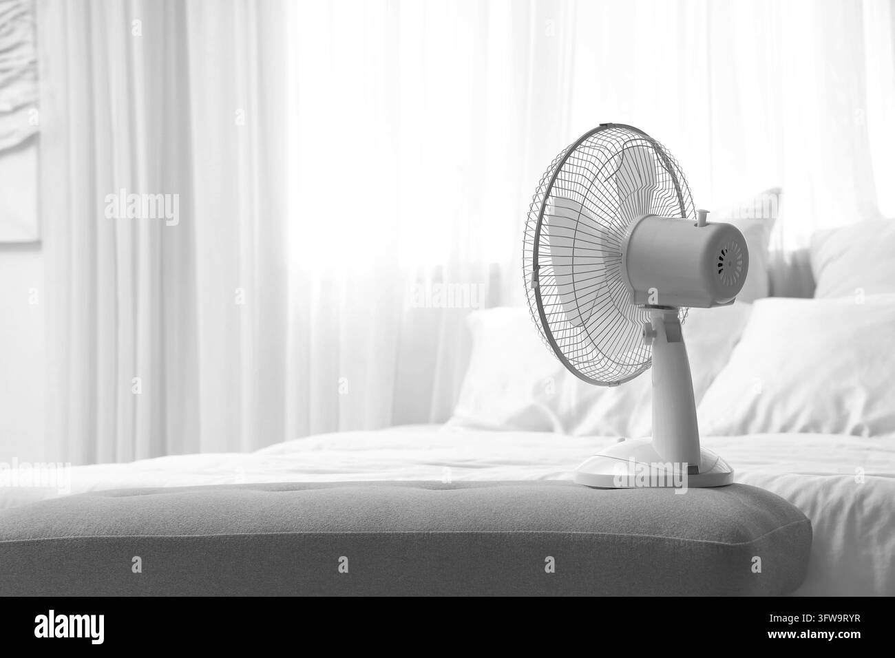 Soulagement des vagues de chaleur et confort estival, ventilateur électrique rafraîchissant l'air dans une chambre lors des fortes chaleurs avec une lumière naturelle vive et une décoration intérieure douce Banque D'Images