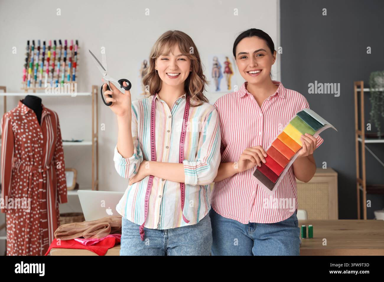 Collaboration en conception de mode, deux couturières travaillant dans un atelier créatif avec des échantillons de tissus et des ciseaux pour la production de vêtements sur mesure Banque D'Images