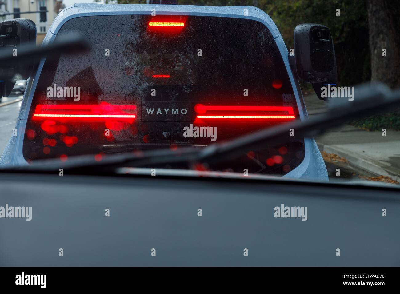 Bellevue, États-Unis - 2 septembre 2026 : Feux arrière rougeoyants et logo Waymo sur un robotaxi autonome, vus depuis une voiture suivante à travers une vitre tachée de pluie Banque D'Images
