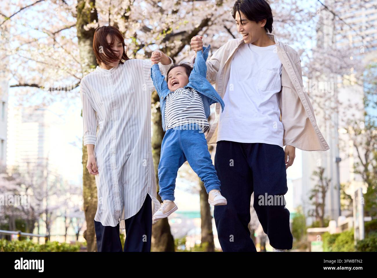 Parents et enfant japonais souriants jouant sous les fleurs de cerisier Banque D'Images