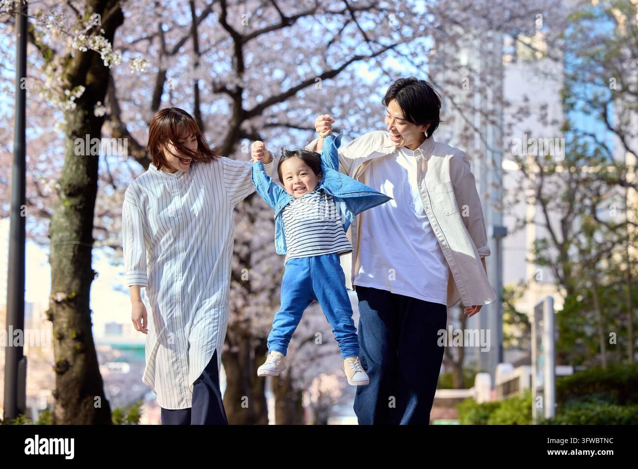 Parent et enfant japonais jouant joyeusement le long d'une rangée de cerisiers Banque D'Images