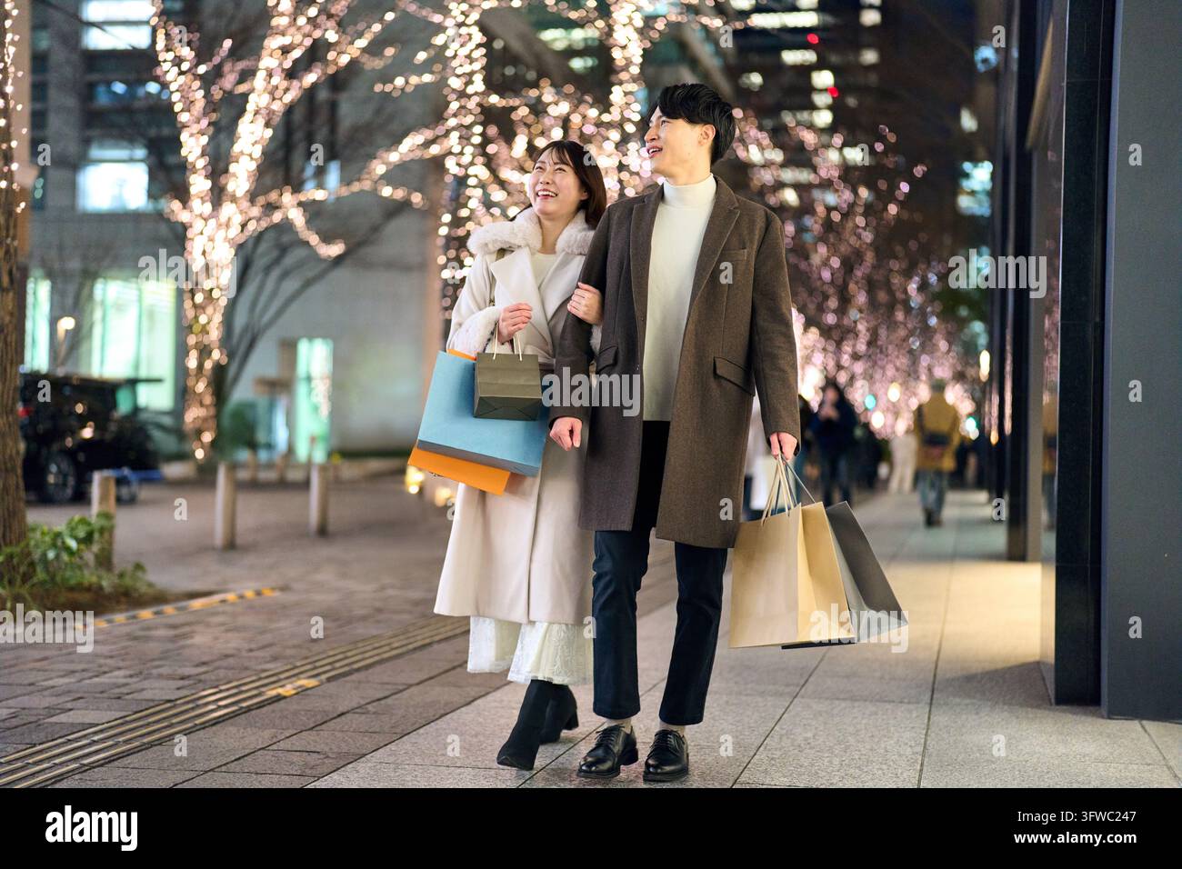 Couple japonais marchant avec le sourire le long d'une rue illuminée par des lumières de fête Banque D'Images