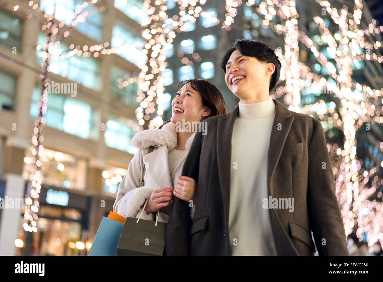 Couple japonais marchant avec des sourires sur leurs visages à travers la ville la nuit illuminée par les lumières Banque D'Images