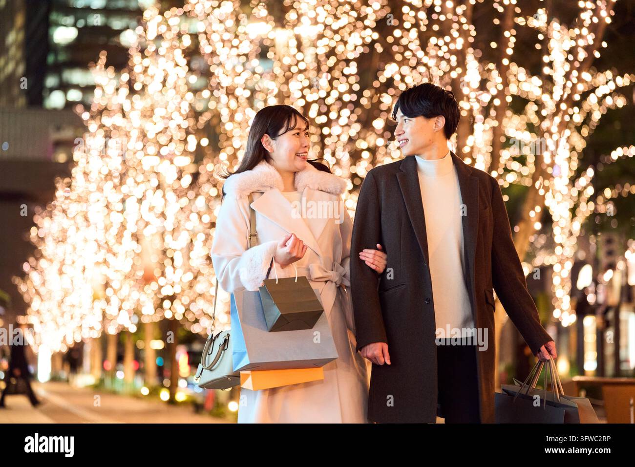 Couple japonais souriant marchant dans une ville illuminée par les lumières des fêtes Banque D'Images