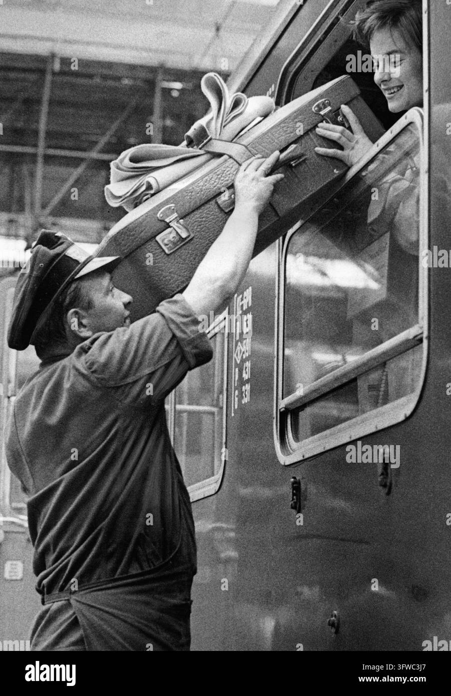 Un agent de manutention des bagages passant une valise par une fenêtre dans un train à la gare centrale de Munich (photographie non datée). [traduction automatisée] Banque D'Images