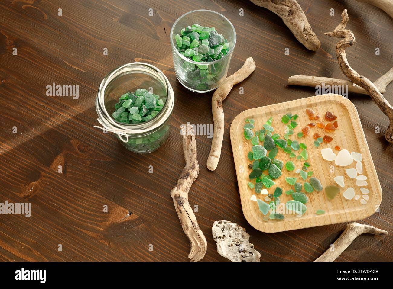 Verre de mer vert dans des bocaux avec du bois flotté sur une table en bois. Flatlay de trésors côtiers triés et de pierres précieuses de plage. Décoration océanique durable zéro déchet et Banque D'Images