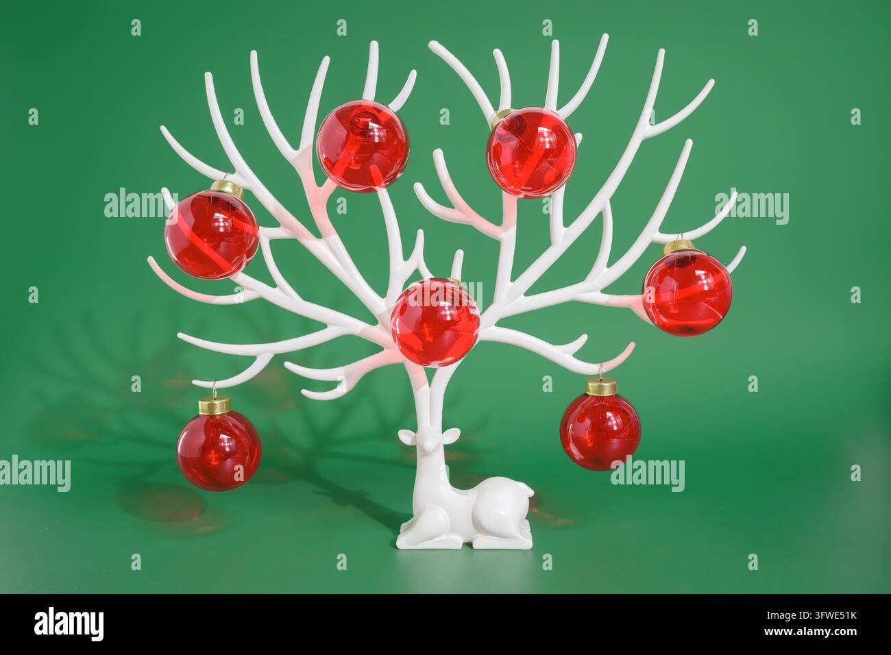 Arbre de Noël blanc sculptural tenant des ornements de boules rouges sur sa forme ramifiée. Cette décoration de table festive associe des sphères brillantes et de l'or c Banque D'Images