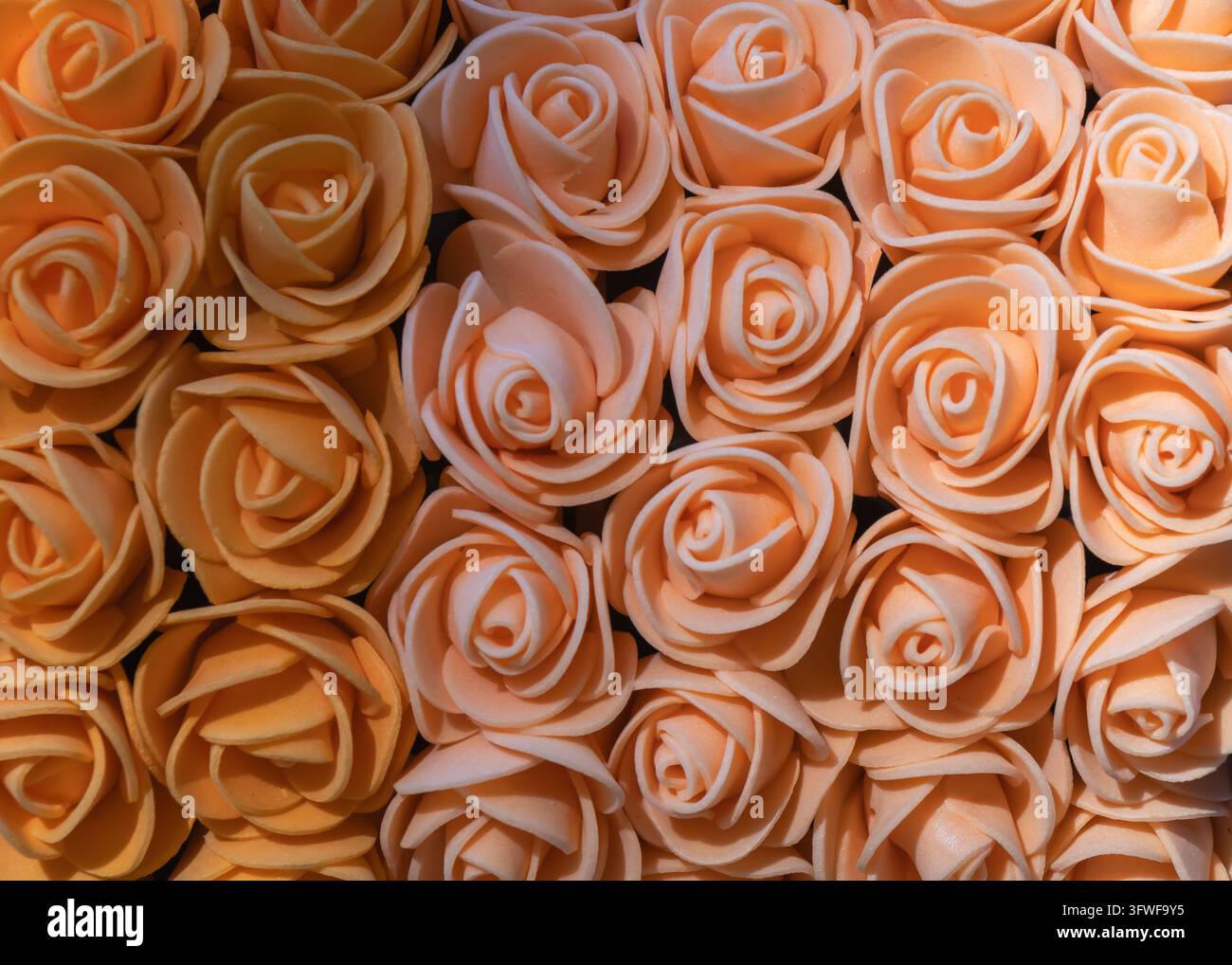 Close-up de nombreuses roses artificielles orange disposées serrées, créant un motif floral décoratif dense avec des pétales doux et un artisanat chaleureux Banque D'Images