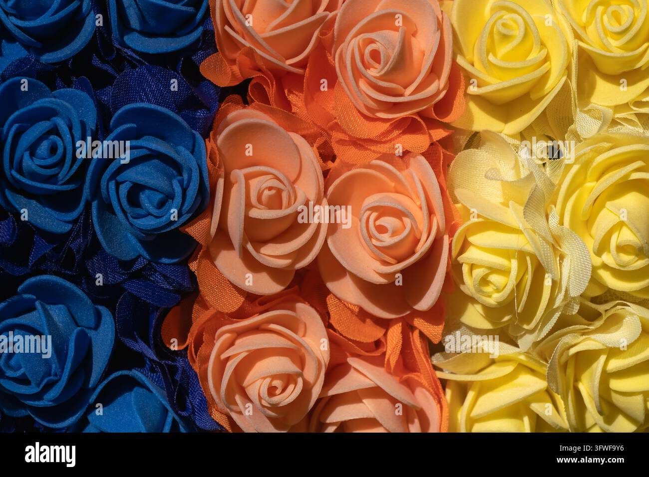 Close-up de roses artificielles en bleu profond, pêche et jaune vif disposées en sections colorées denses, créant un motif floral décoratif vibrant et Banque D'Images