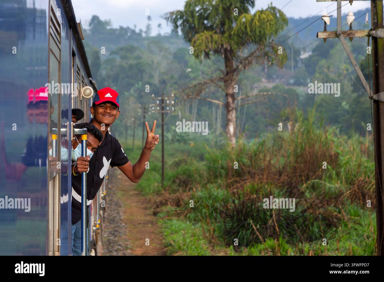 Jeunes hommes se penchant par la fenêtre d'un train en faisant un signe de victoire, province d'Uva, Ella, Sri Lanka Banque D'Images