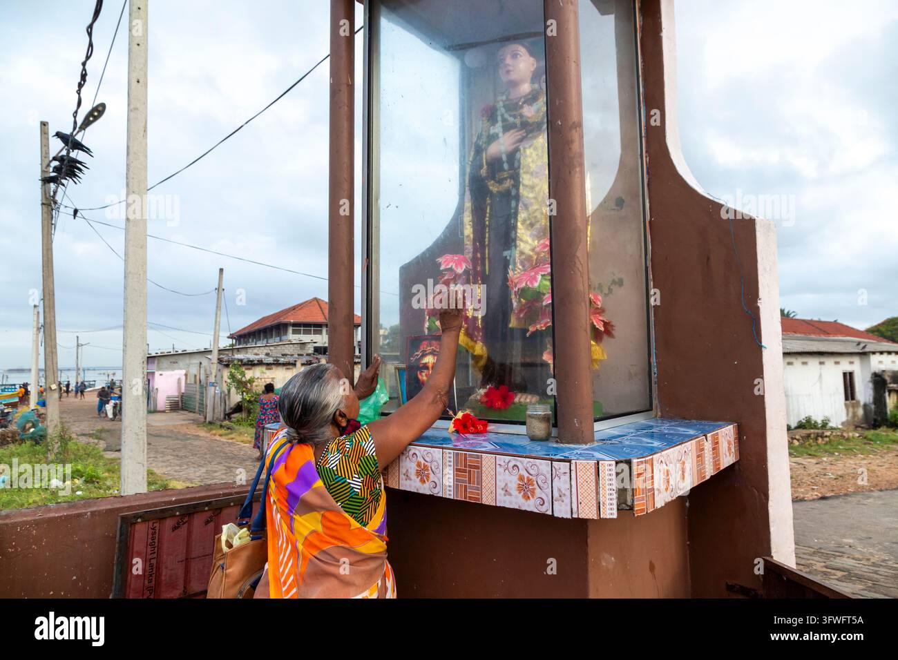 Femme touchant la vitrine en verre d'une statue chrétienne en prière, Province du Nord, Jaffna, Sri Lanka Banque D'Images