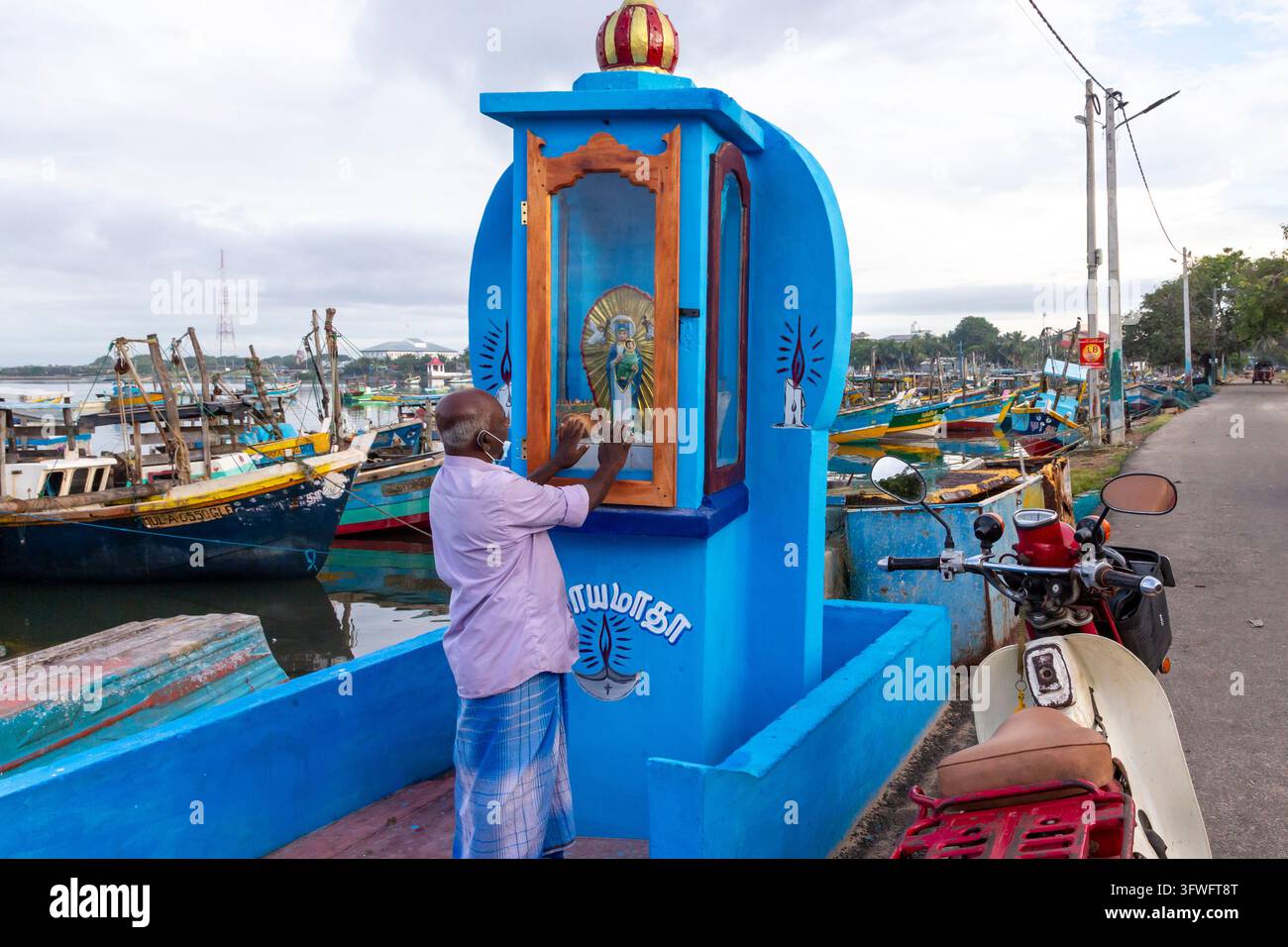Homme priant à un sanctuaire chrétien bleu à côté d'un port de pêche, Province du Nord, Jaffna, Sri Lanka Banque D'Images