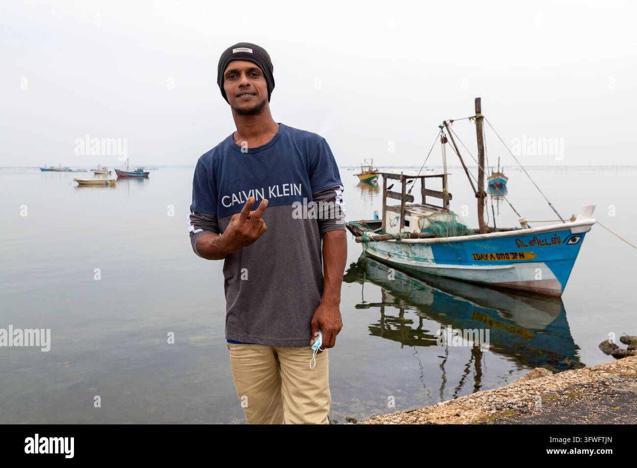 Jeune homme faisant un signe de paix à côté d'un bateau de pêche, Province du Nord, Jaffna, Sri Lanka Banque D'Images