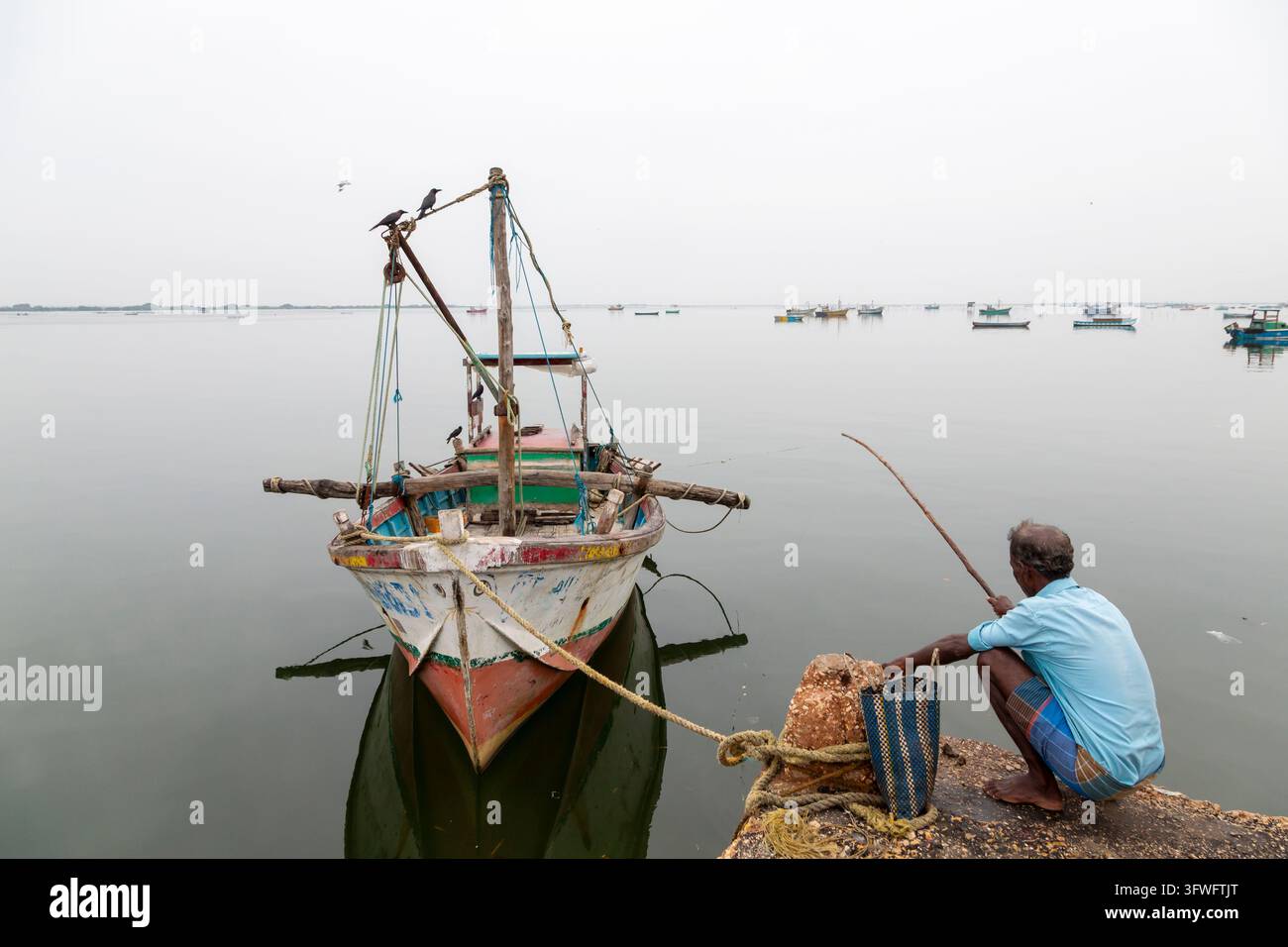 Homme pêchant avec une canne à pêche à côté d'un bateau en bois amarré, Province du Nord, Jaffna, Sri Lanka Banque D'Images