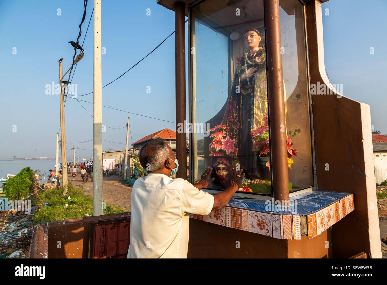 Homme priant les mains posées sur le verre d’un sanctuaire routier chrétien, Province du Nord, Jaffna, Sri Lanka Banque D'Images