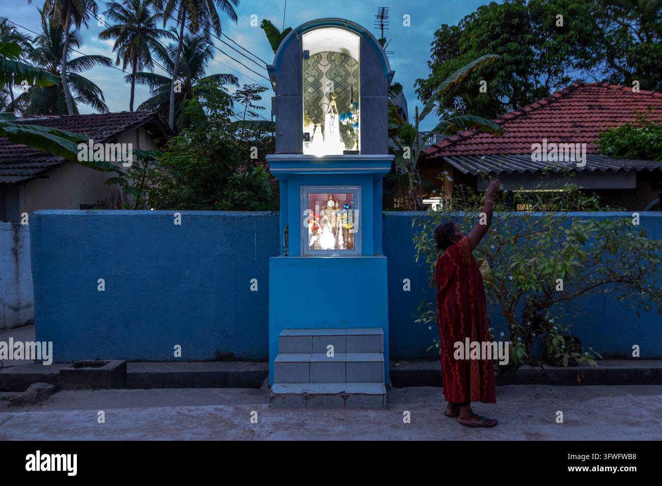 Femme touchant un autel routier chrétien bleu au crépuscule, Province occidentale, Negombo, Sri Lanka Banque D'Images