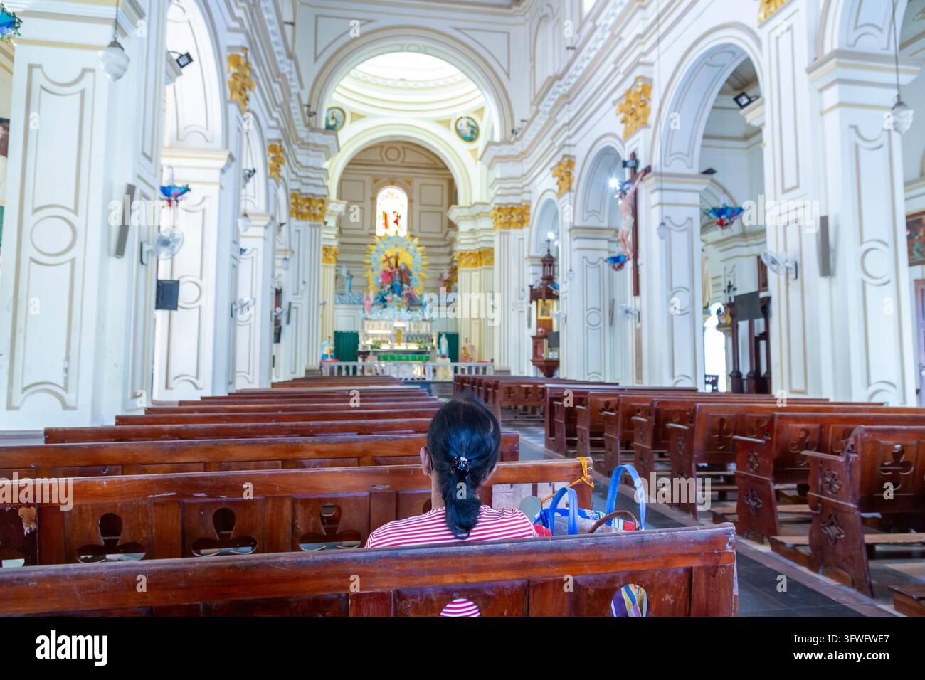 Femme assise seule dans les bancs d'une grande église catholique blanche, province occidentale, Negombo, Sri Lanka Banque D'Images