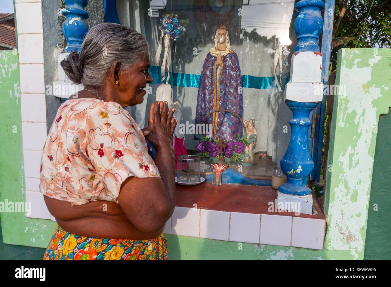 Ancienne femme priant devant un sanctuaire routier de la Vierge Marie, Province occidentale, Negombo, Sri Lanka Banque D'Images