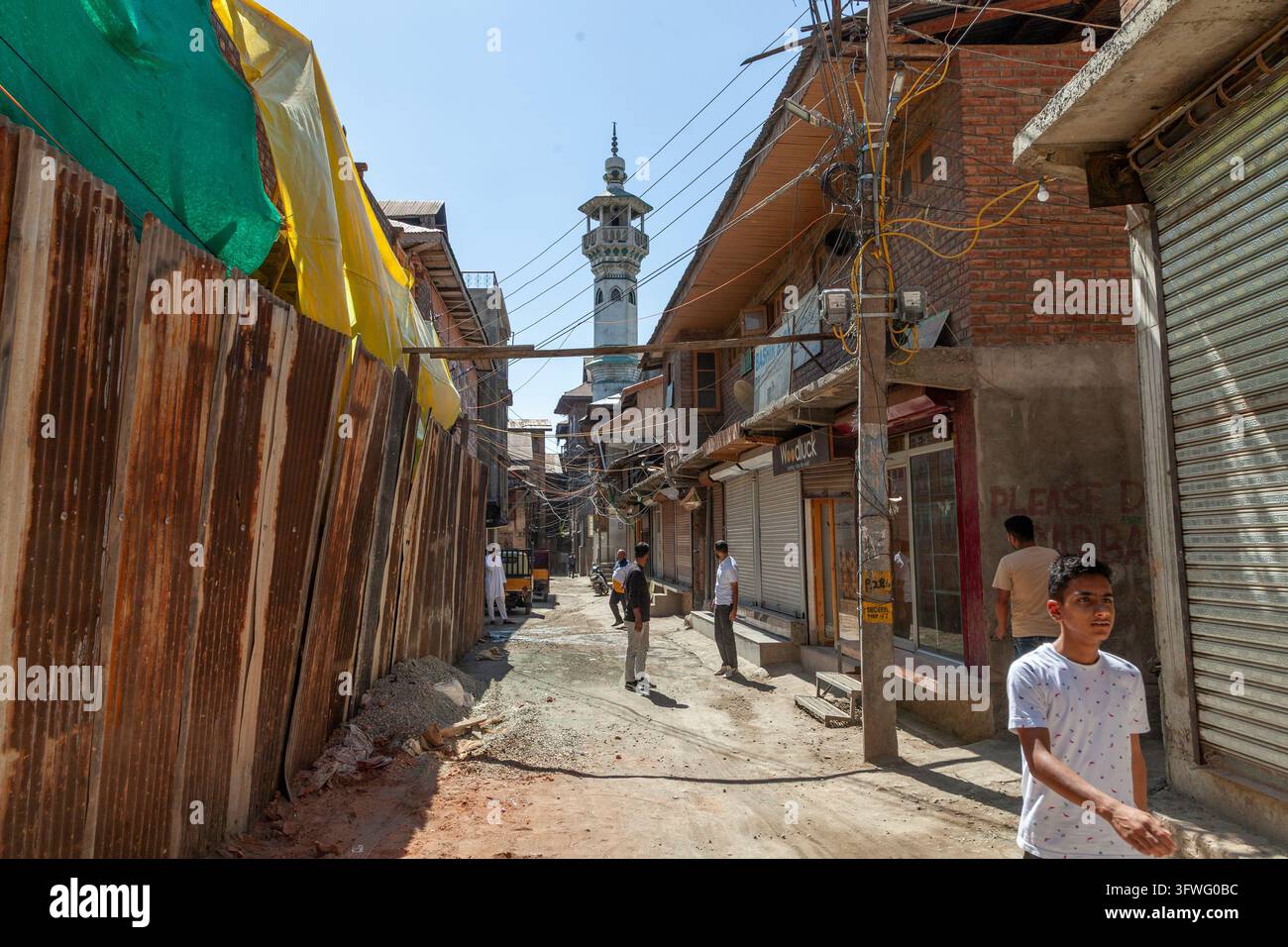 Rue étroite de vieille ville avec clôture en tôle ondulée et minaret de mosquée, Jammu et Cachemire, Srinagar, Inde Banque D'Images