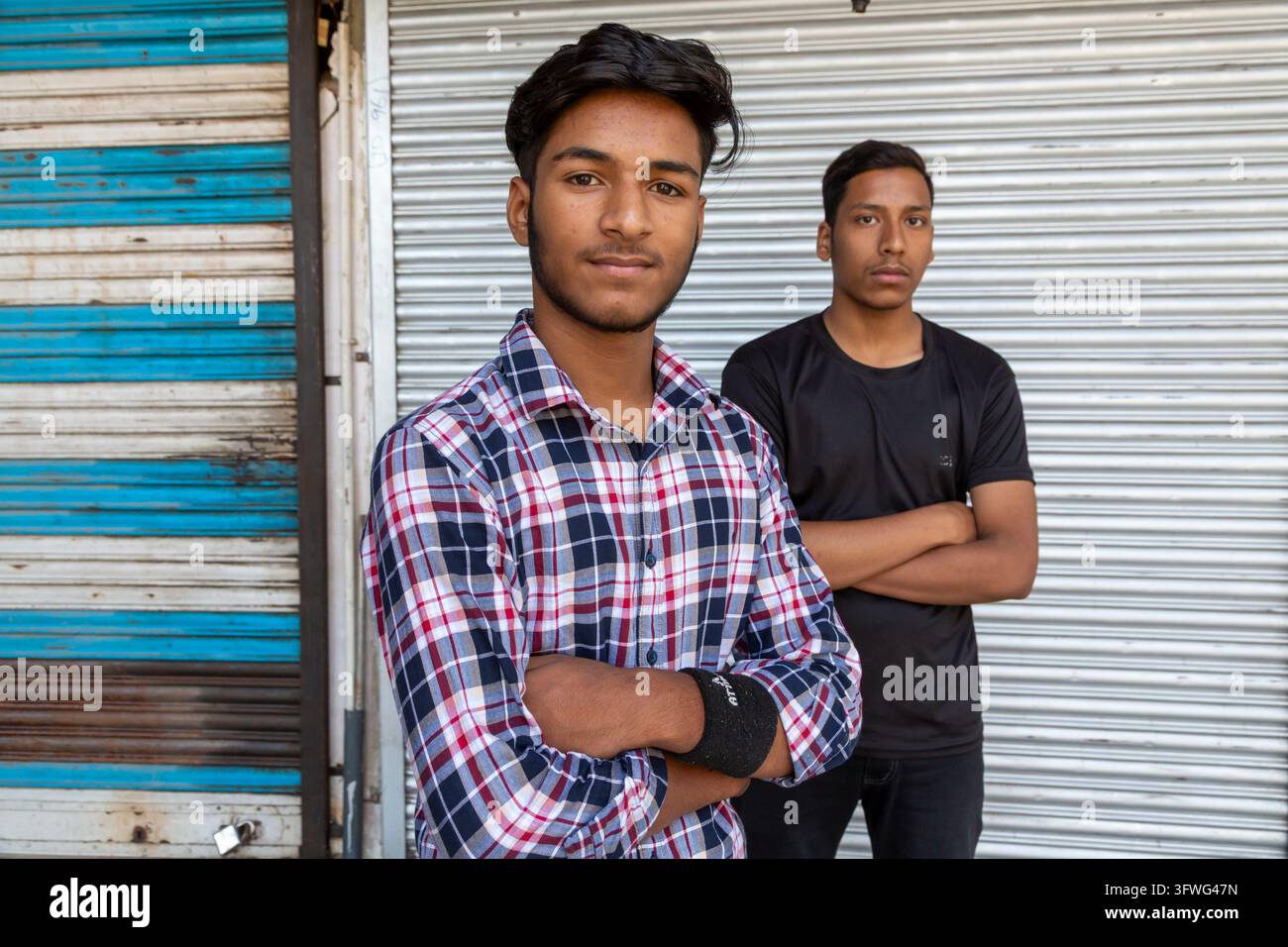 Deux jeunes hommes aux bras croisés debout devant une grille métallique, Jammu-et-Cachemire, Srinagar, Inde Banque D'Images