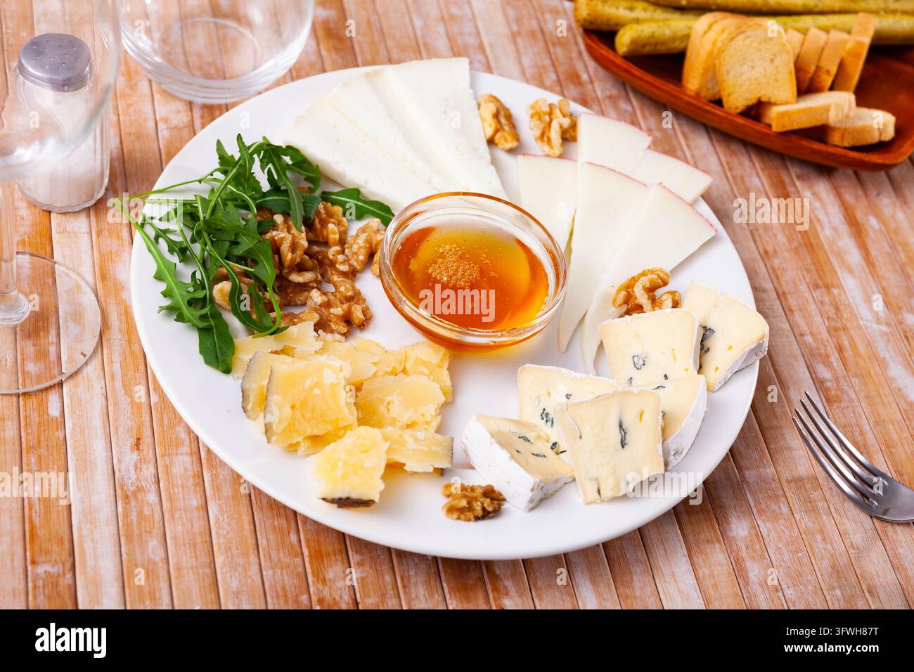 Différents types de fromage tranchés et servis dans une assiette avec un bol de miel, des noix et de la roquette Banque D'Images
