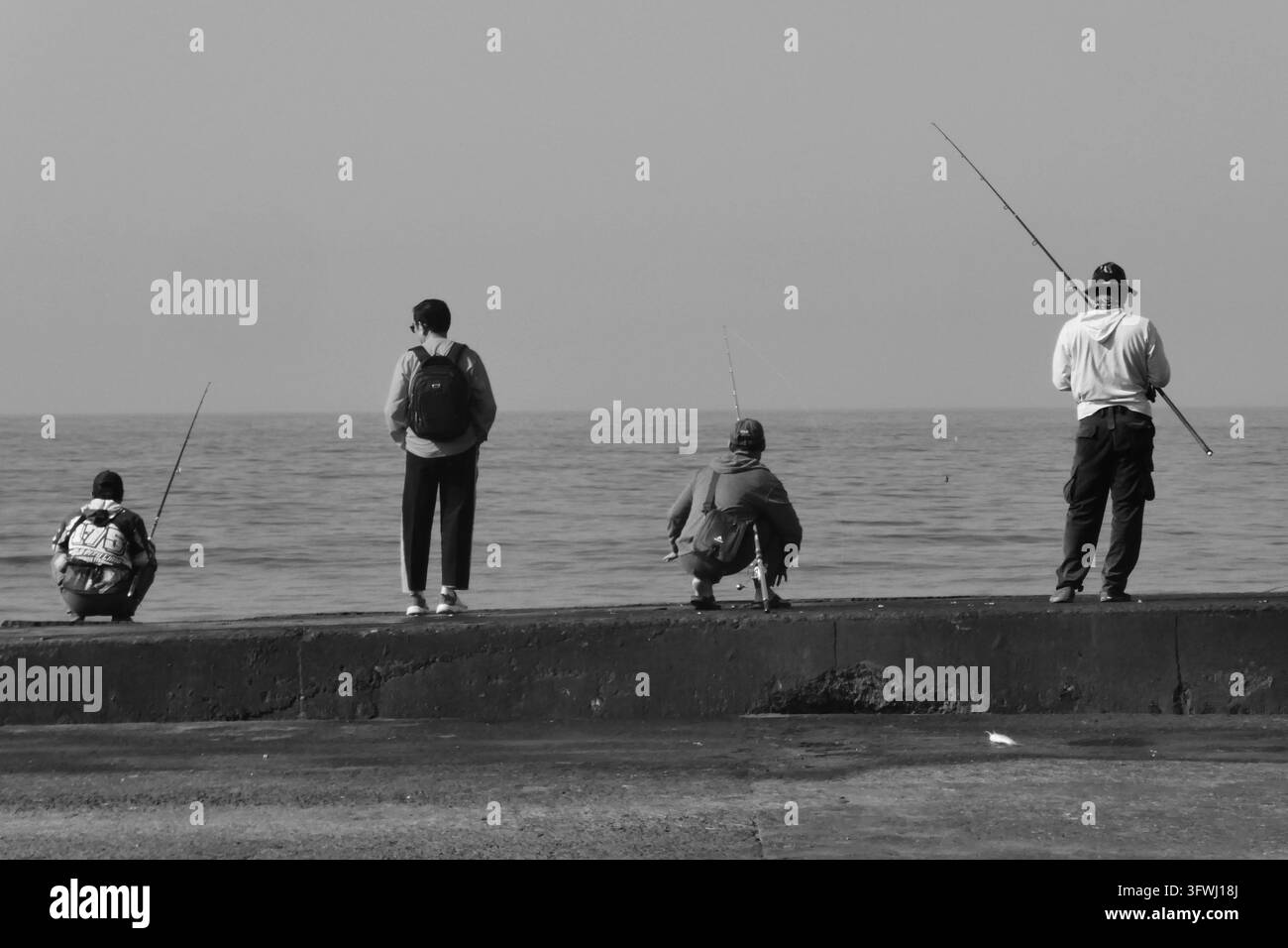 Photographie en noir et blanc d'hommes pêchant depuis une jetée, profitant des loisirs en plein air à l'horizon calme de la mer Banque D'Images