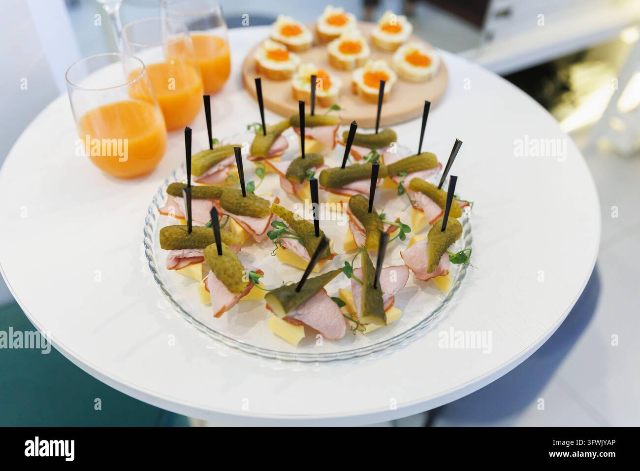 Close-up de canapés gourmands au concombre et aux légumes disposés sur une assiette blanche avec des boissons aux agrumes en arrière-plan pour un service d'événement élégant Banque D'Images