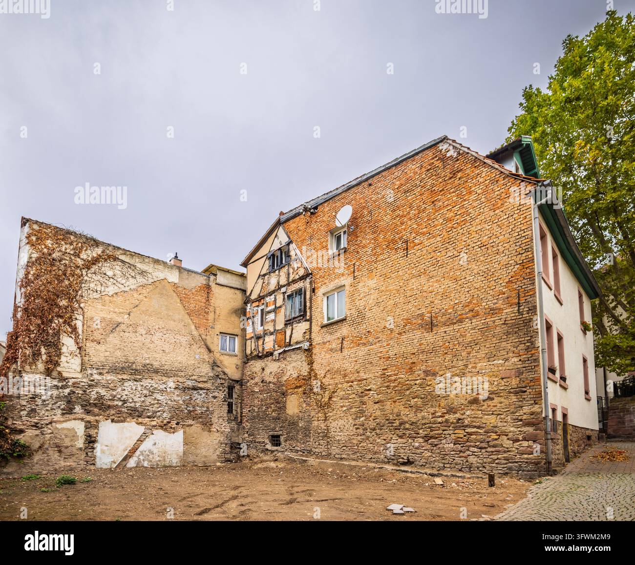 Des bâtiments en briques érodés et des ruines exposées encadrent une cour historique tranquille sous un ciel nuageux Banque D'Images