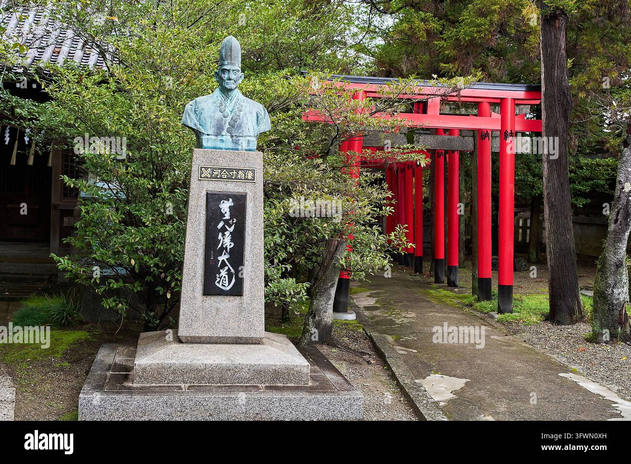 Buste en bronze d'une figure historique japonaise à côté de portes torii rouges dans un sanctuaire shintoïste traditionnel entouré d'arbres au Japon. Banque D'Images